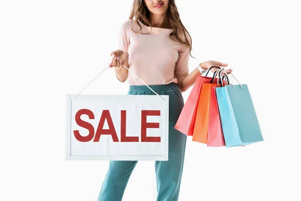 Vista recortada de la mujer que sostiene el tablero con el letrero de la venta y bolsas de compras, aislado en blanco - foto de stock