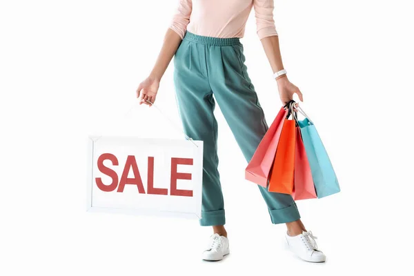 Vista recortada de la hermosa chica que sostiene el tablero con el cartel de la venta y bolsas de compras, aislado en blanco - foto de stock
