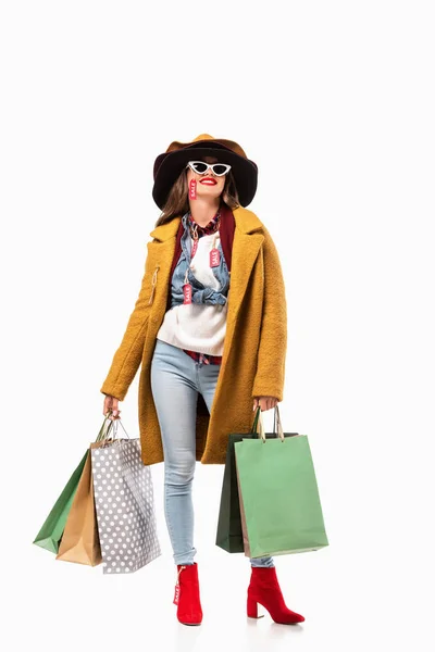 Chica sonriente en traje de otoño con etiquetas de venta sosteniendo bolsas de compras, aislado en blanco - foto de stock