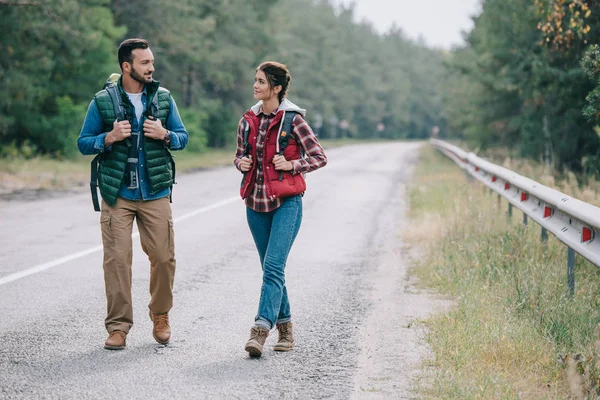 Couple of travelers with backpacks walking on road — Stock Photo