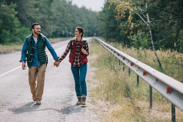 Casal de viajantes com mochilas de mãos dadas enquanto caminhava na estrada — Fotografia de Stock