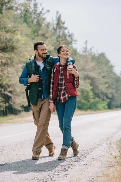Couple of travelers with backpacks walking on road — Stock Photo