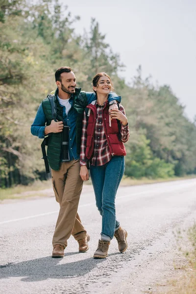 Pareja de viajeros con mochilas caminando por la carretera - foto de stock