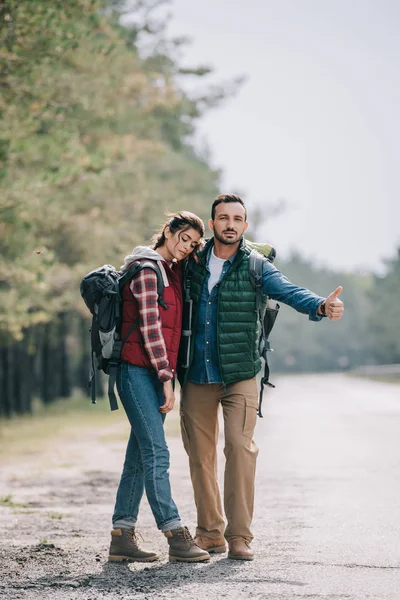 Couple of travelers with backpacks hitchhiking on road — Stock Photo