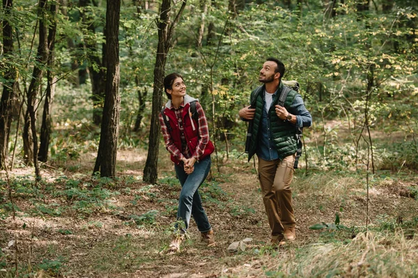 Пара усміхнених мандрівників з рюкзаками, що ходять у лісі — стокове фото