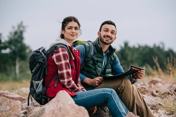 Side view of hikers with map and backpacks sitting on rocks on sandy beach — Stock Photo