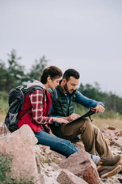 Side view of hikers looking for destination on map while sitting on rocks on sandy beach — Stock Photo