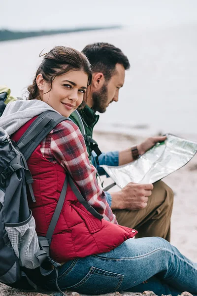 Vue latérale des randonneurs avec carte assise sur des rochers sur une plage de sable fin — Photo de stock