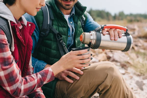 Vue partielle du couple de voyageurs avec boisson chaude dans le thermos — Photo de stock