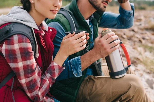 Обрезанный снимок парочки путешественников с горячим напитком в термосе — стоковое фото