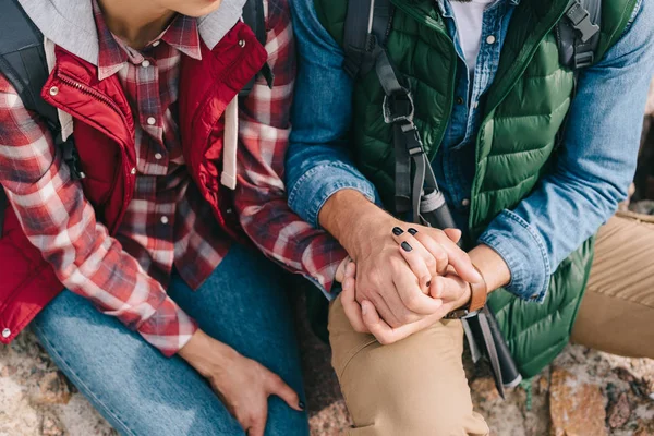 Teilansicht von Reisenden, die sich Händchen haltend auf Felsen am Sandstrand ausruhen — Stockfoto