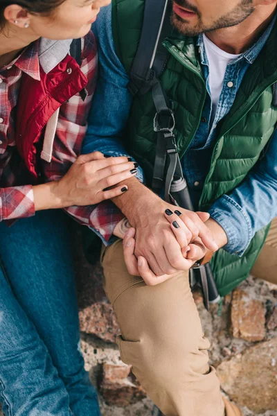 Partial view of couple of travelers holding hands while resting on rocks on sandy beach — Stock Photo