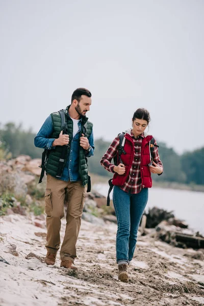 Hikers with backpacks walking on sandy beach together — Stock Photo