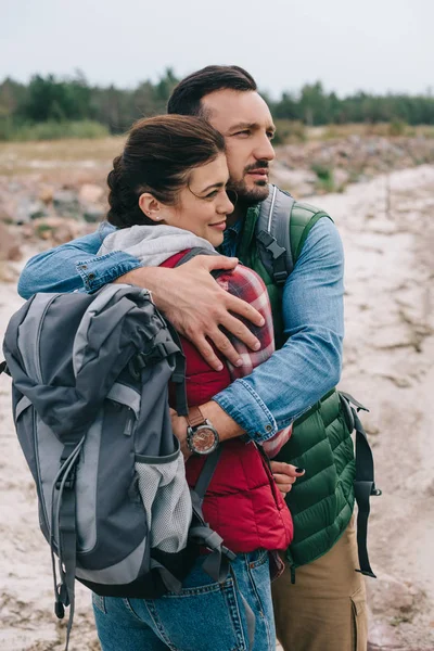 Couple of hikers with backpacks hugging on sandy beach — Stock Photo