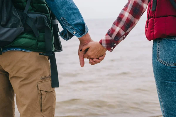 Cropped shot of couple holding hands while standing at sea — Stock Photo