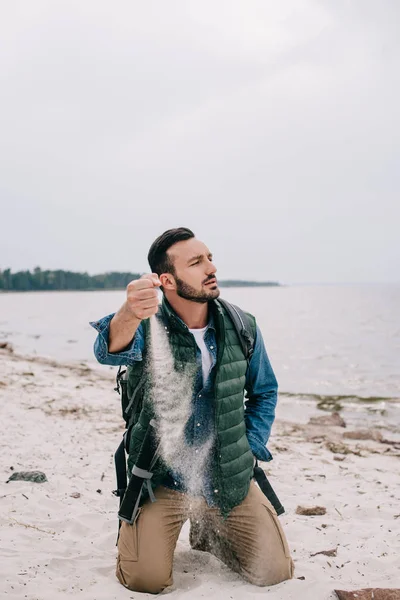 Uomo con zaino versando sabbia sulla spiaggia — Foto stock