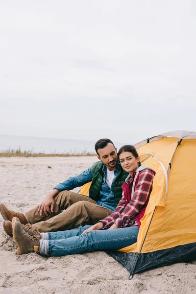 Vista lateral do casal sentado na barraca de acampamento na praia de areia — Fotografia de Stock