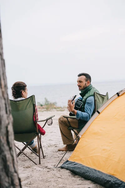 Homme jouant guitare acoustique pour femme sur camping — Photo de stock