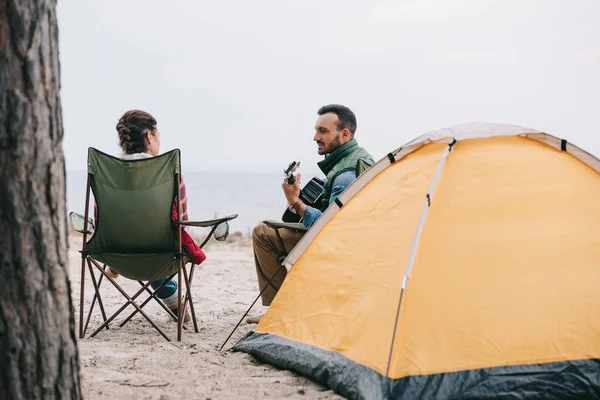 Hombre tocando la guitarra acústica para la esposa en camping - foto de stock