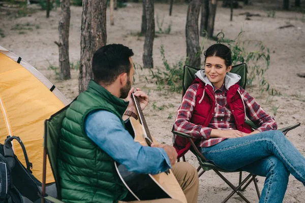 Man playing acoustic guitar for smiling wife on camping — Stock Photo