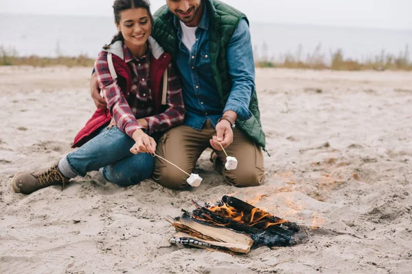 Feliz pareja asando malvavisco en hoguera en la playa de arena - foto de stock