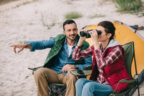 Woman looking through binoculars while having camping together with husband on sandy beach — Stock Photo