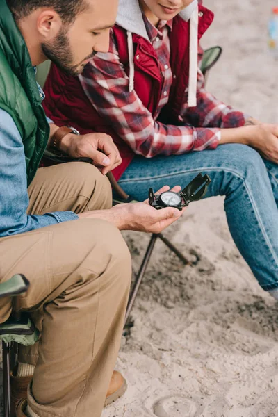 Vista parcial do casal com bússola sentado em cadeiras ao ter camping — Fotografia de Stock