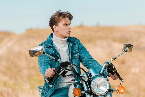 Young man sitting on retro motorbike on rural meadow — Stock Photo