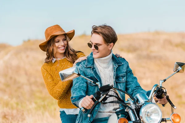 Jovem namorada olhando namorado sentado em moto no prado rural — Fotografia de Stock