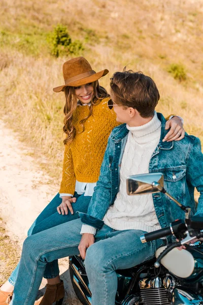 Couple élégant assis sur moto rétro et regardant l'autre sur prairie rurale — Photo de stock