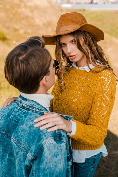 Beautiful girlfriend looking at camera and hugging boyfriend on meadow — Stock Photo