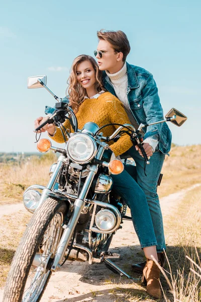 Sonriente novia sentado en moto mientras novio mirando lejos en prado - foto de stock