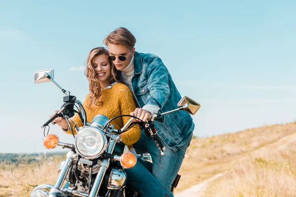 Jeune couple à la recherche de moto vintage sur prairie rurale — Photo de stock