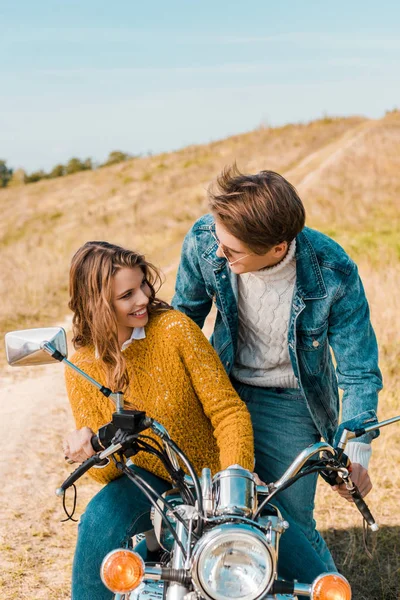Jovem casal sentado em moto e sorrindo um para o outro — Fotografia de Stock