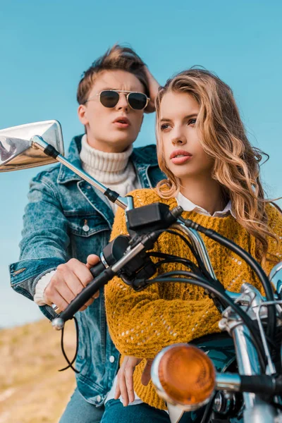 Молодая пара, сидящая на мотоцикле против голубого неба — стоковое фото