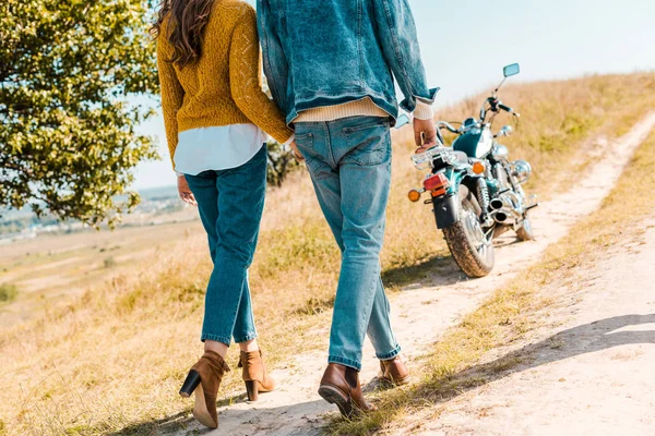 Vista cortada do casal andando no prado rural e moto no fundo — Fotografia de Stock