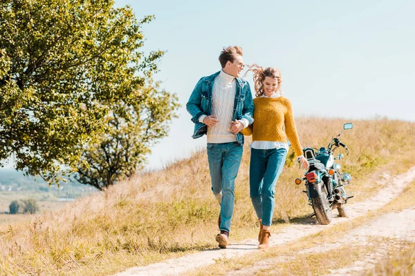 Glückliches Paar läuft mit Motorrad im Hintergrund über Wiese — Stockfoto