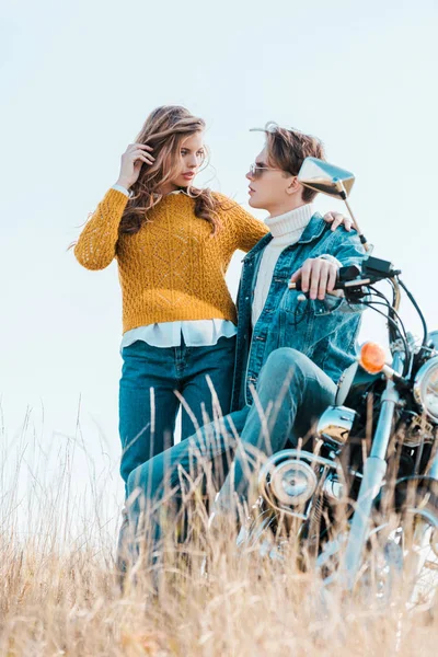 Молодая пара смотрит друг на друга и стоит рядом с мотоциклом — стоковое фото