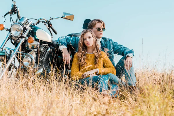 Молодой парень и девушка, сидя рядом с мотоциклом на лугу — стоковое фото