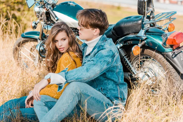 Jovem casal sentado perto de moto vintage no prado — Fotografia de Stock