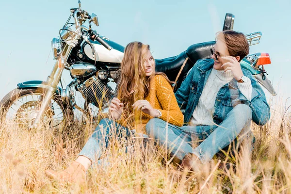 Feliz pareja sentado cerca de moto vintage y mirándose el uno al otro - foto de stock