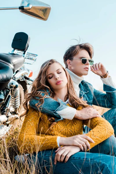 Молодой парень обнимает девушку и сидит рядом с винтажным мотоциклом — стоковое фото