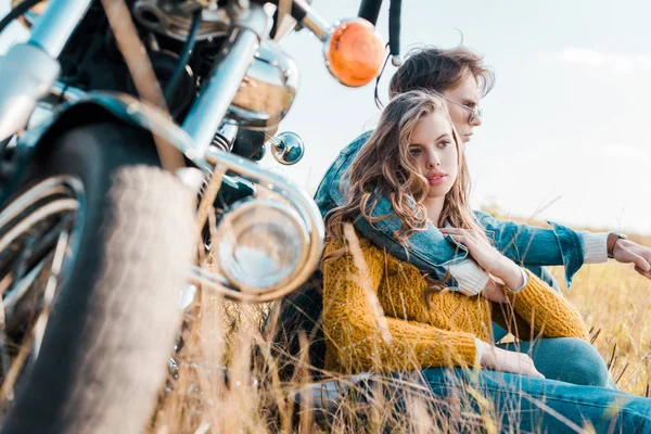 Namorado abraçando namorada e sentado perto de motocicleta vintage — Fotografia de Stock