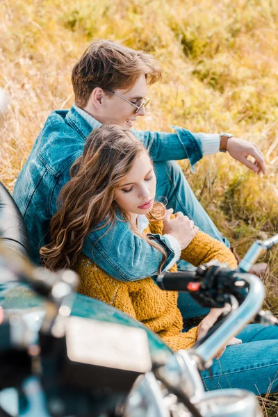 Guapo novio abrazando novia y sentado cerca de vintage moto - foto de stock