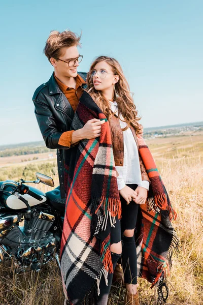 Jovem casal em óculos de pé perto de motocicleta vintage e olhando um para o outro — Fotografia de Stock