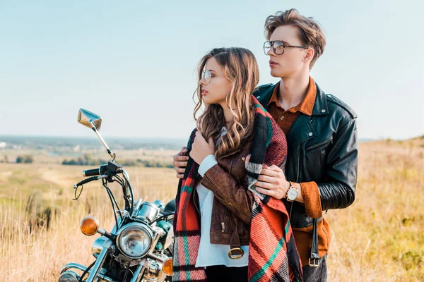 Пара в очках глядя в сторону и стоя рядом с ретро мотоцикл — стоковое фото