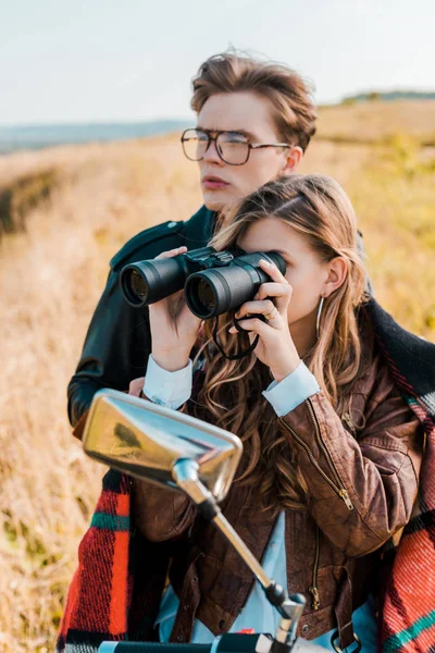 Girlfriend looking through binoculars near handsome boyfriend sitting on motorbike — Stock Photo