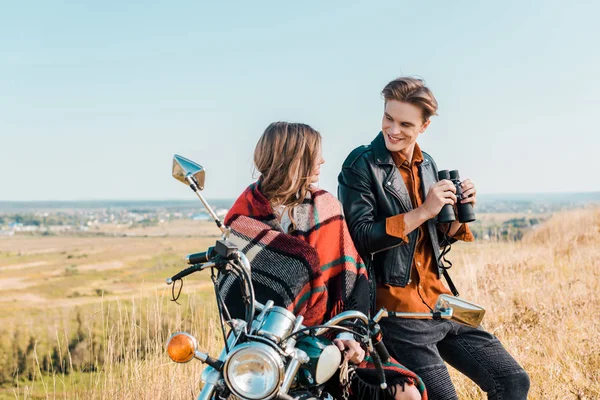 Молодий хлопець тримає бінокль біля дівчини, сидячи на мотоциклі — стокове фото