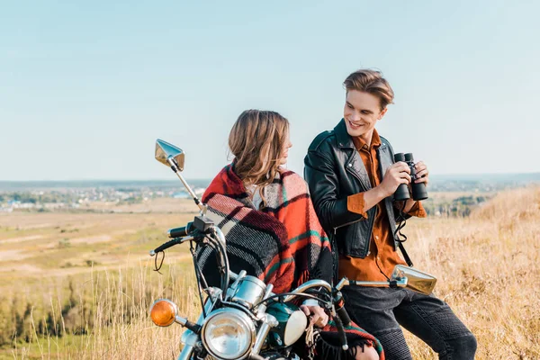 Joven novio sosteniendo prismáticos cerca de novia sentado en moto - foto de stock