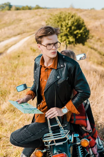 Hermoso viajero en gafas sosteniendo mapa cerca de hermosa novia sentado en moto vintage - foto de stock